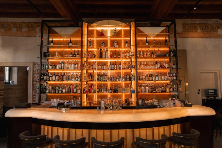 Velvet’s curved bar with amber-lit shelves of spirits beneath exposed wooden ceiling beams.