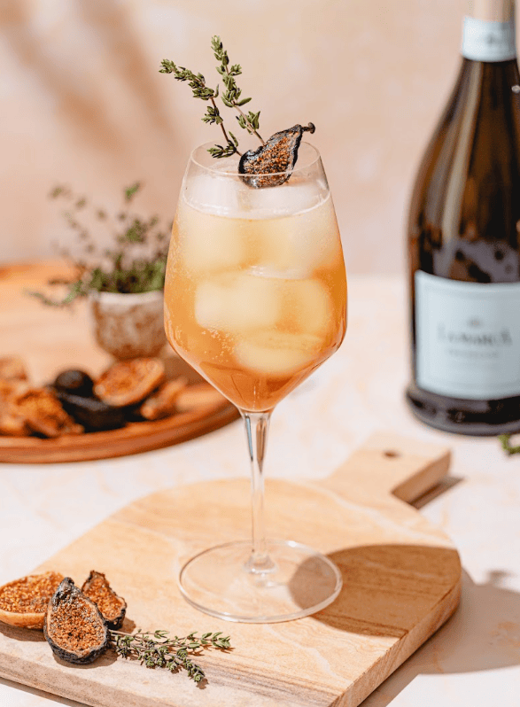 Fig spritz over ice garnished with a fig slice and thyme beside a bottle of La Marca Prosecco