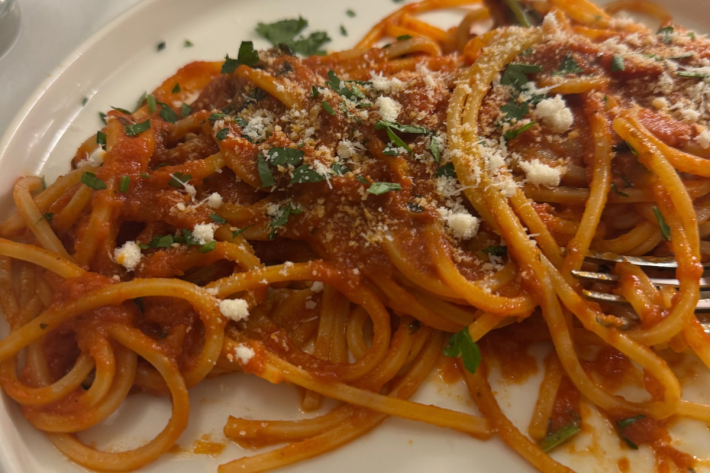 Chitarra pasta with tomato sauce, grated cheese and herbs on a white plate.