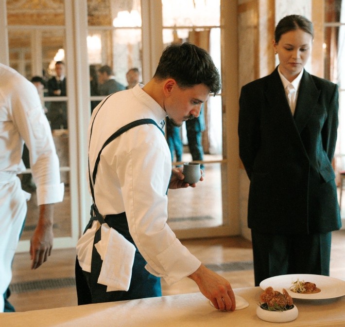 Chef Gennaro Liguori arranging tableware beside plated dishes as a staff member watches.