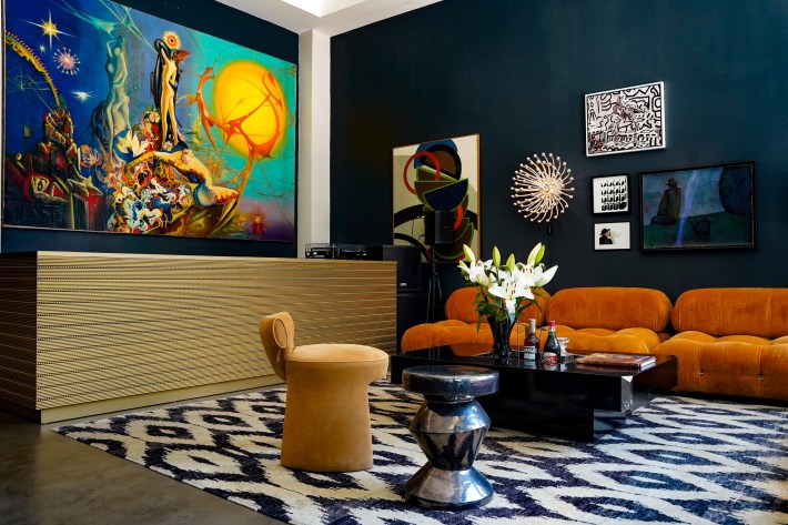 Hotel Trieste lobby with colorful paintings, an orange sofa, a gold reception desk and a patterned rug.