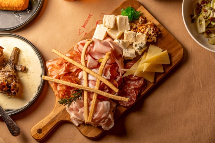 Cured meats, assorted cheeses, breadsticks and walnuts on a wooden board.
