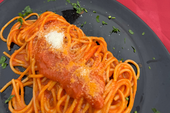 Spaghetti with tomato sauce, grated cheese and basil on a black plate.