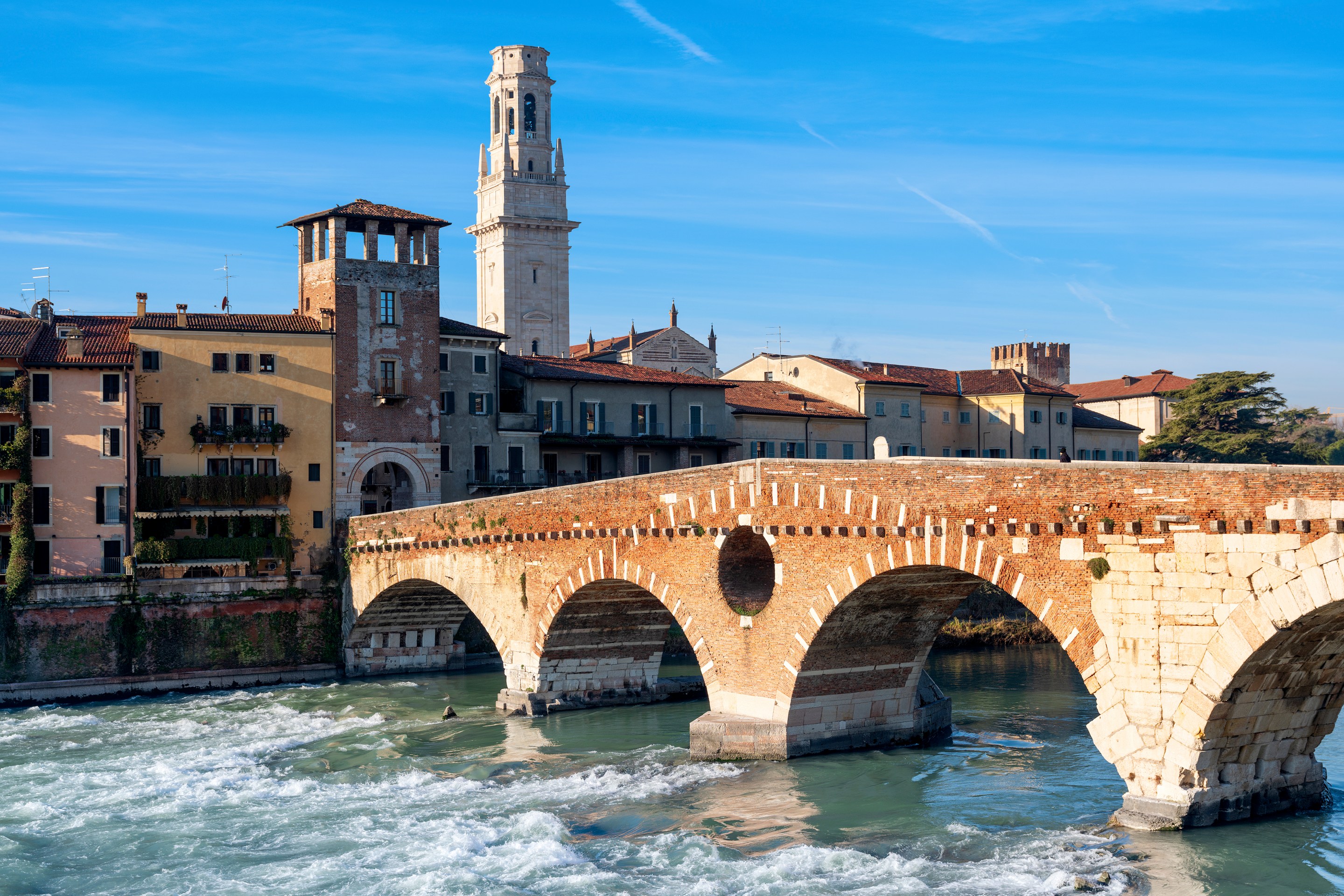 Ponte Pietra’s stone and brick arches cross the Adige River, with Verona’s buildings and a bell tower behind it.