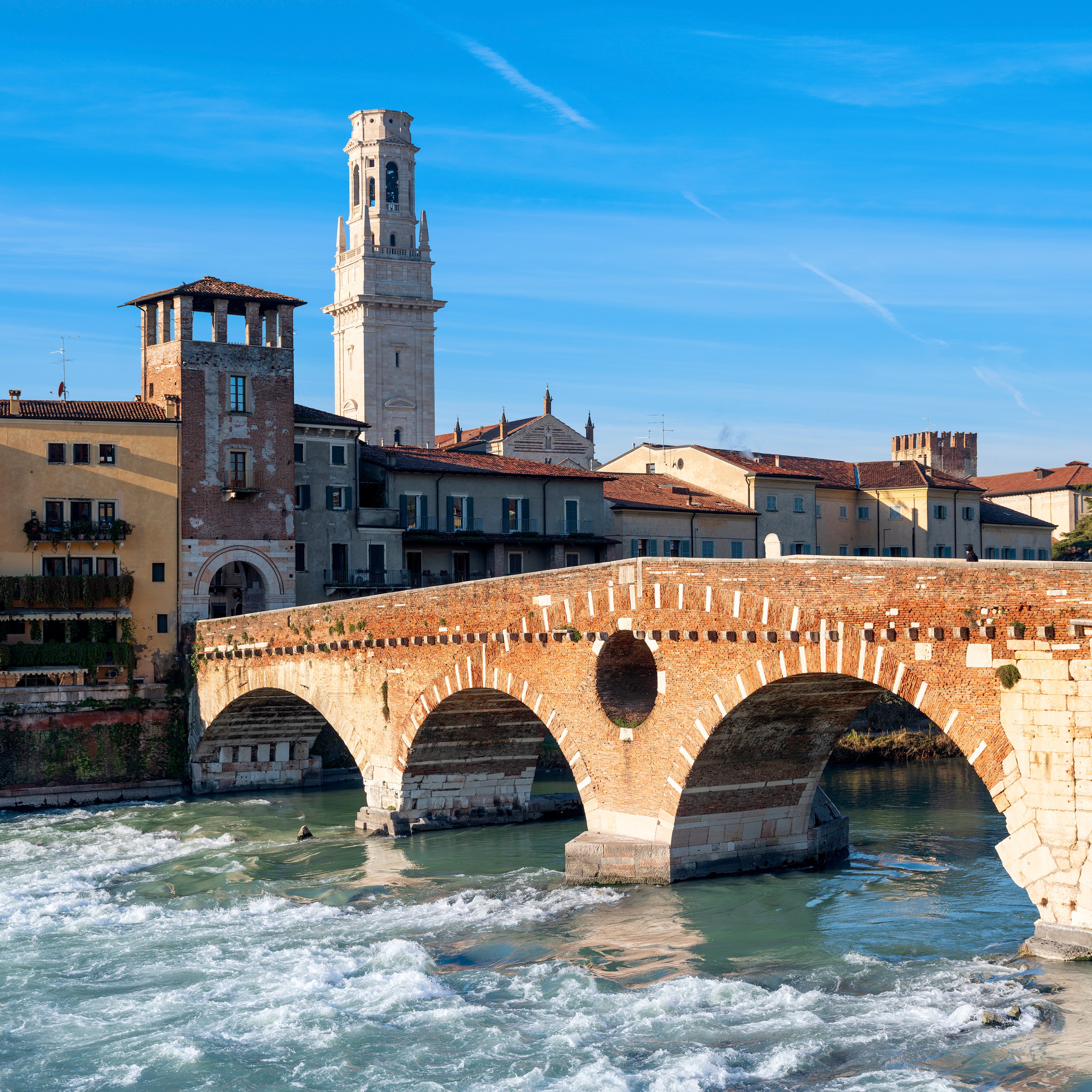 Ponte Pietra’s stone and brick arches cross the Adige River, with Verona’s buildings and a bell tower behind it.